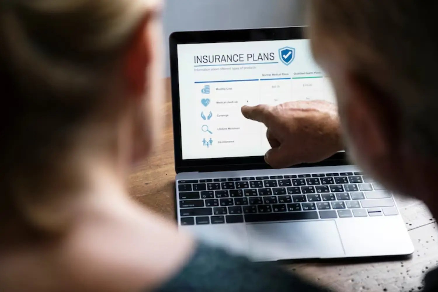 Two individuals discuss insurance plans displayed on a laptop, with one pointing at the screen highlighting various coverage options.